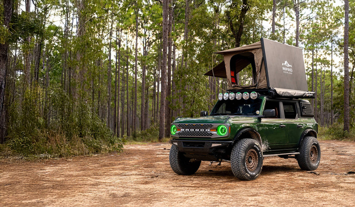 Toyota Tacoma with an aftermarket front bumper, roof rack, rock sliders and auxiliary lights on a dirt trail