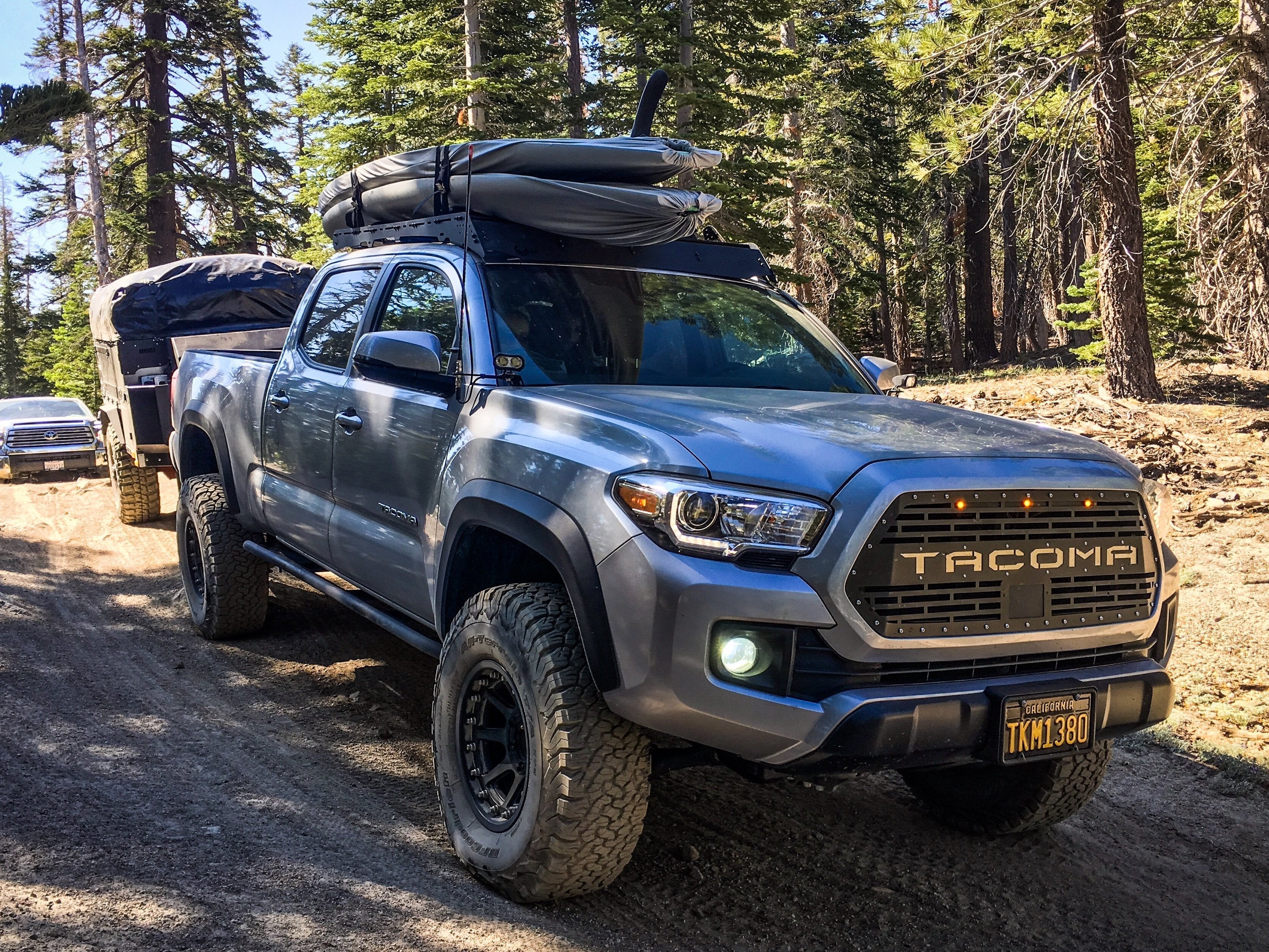 Toyota Tacoma overlanding truck with camping gear and trailer on a forest trail