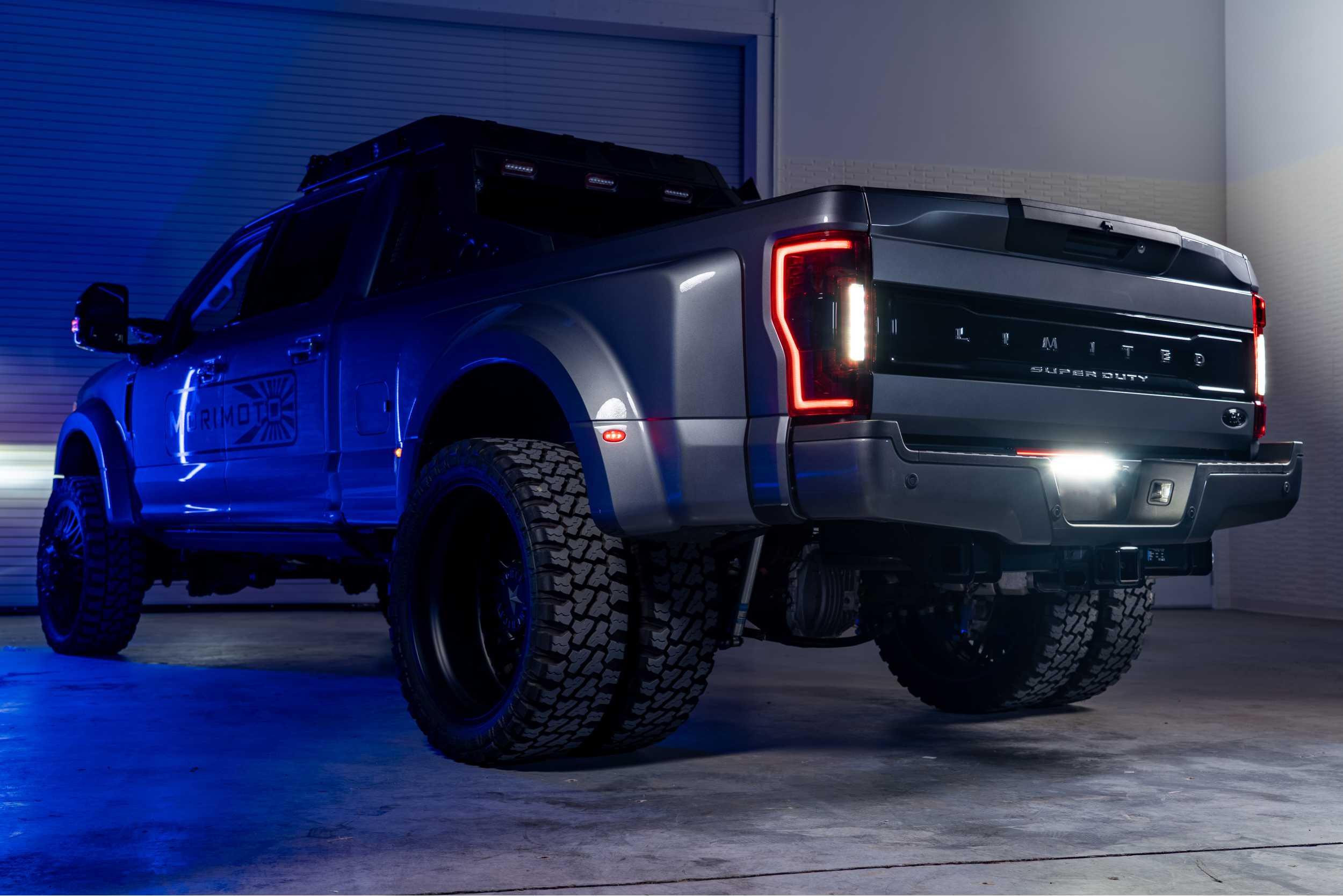 Lifted Ford Super Duty pickup truck with off-road tires and LED tail lights in a garage