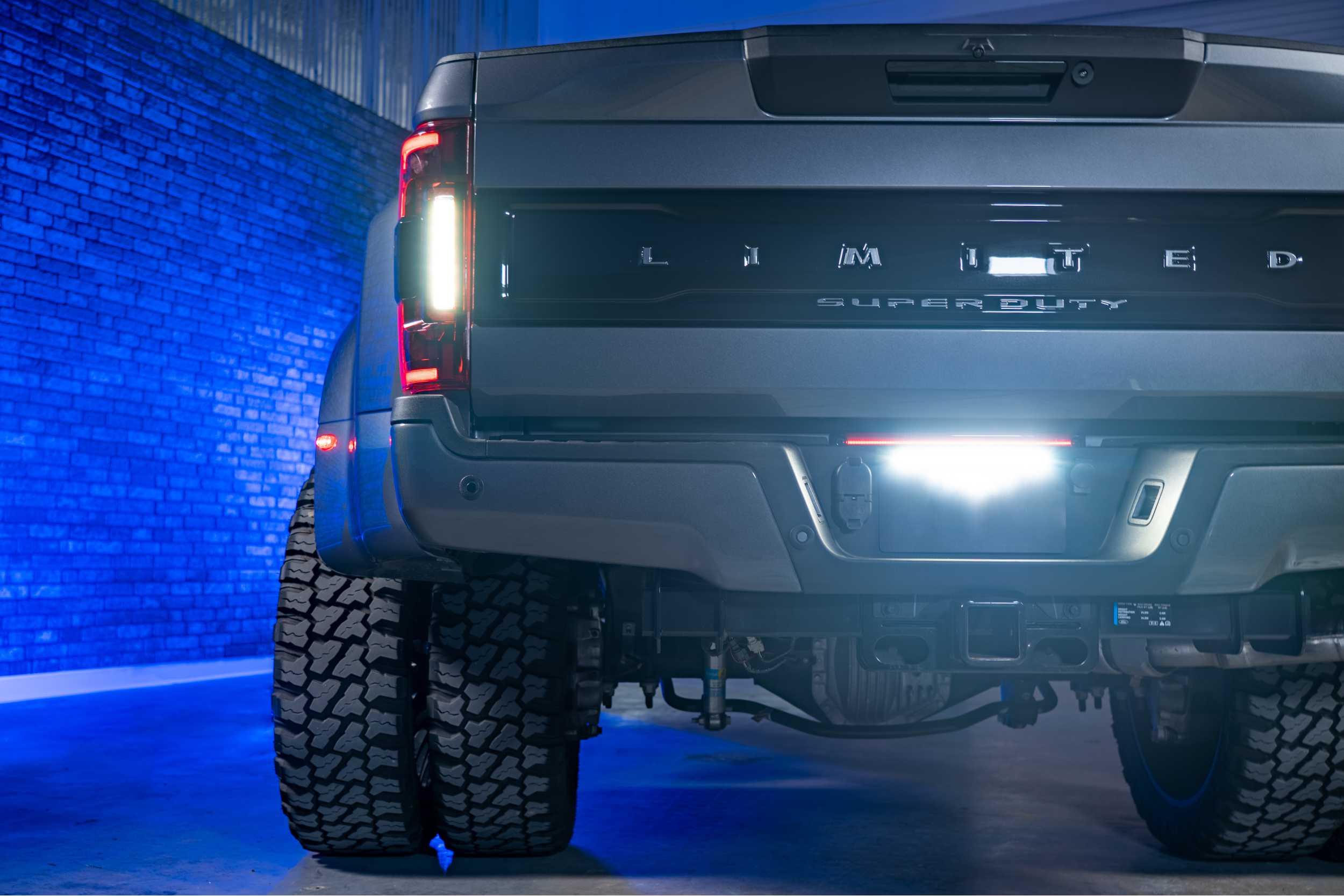 Rear view of a lifted truck with off-road tires and illuminated tailgate in a blue-lit garage.