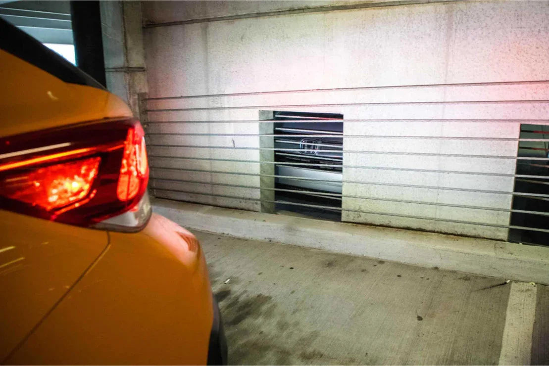 Close-up of orange SUV taillight in indoor parking garage with concrete wall and bars.