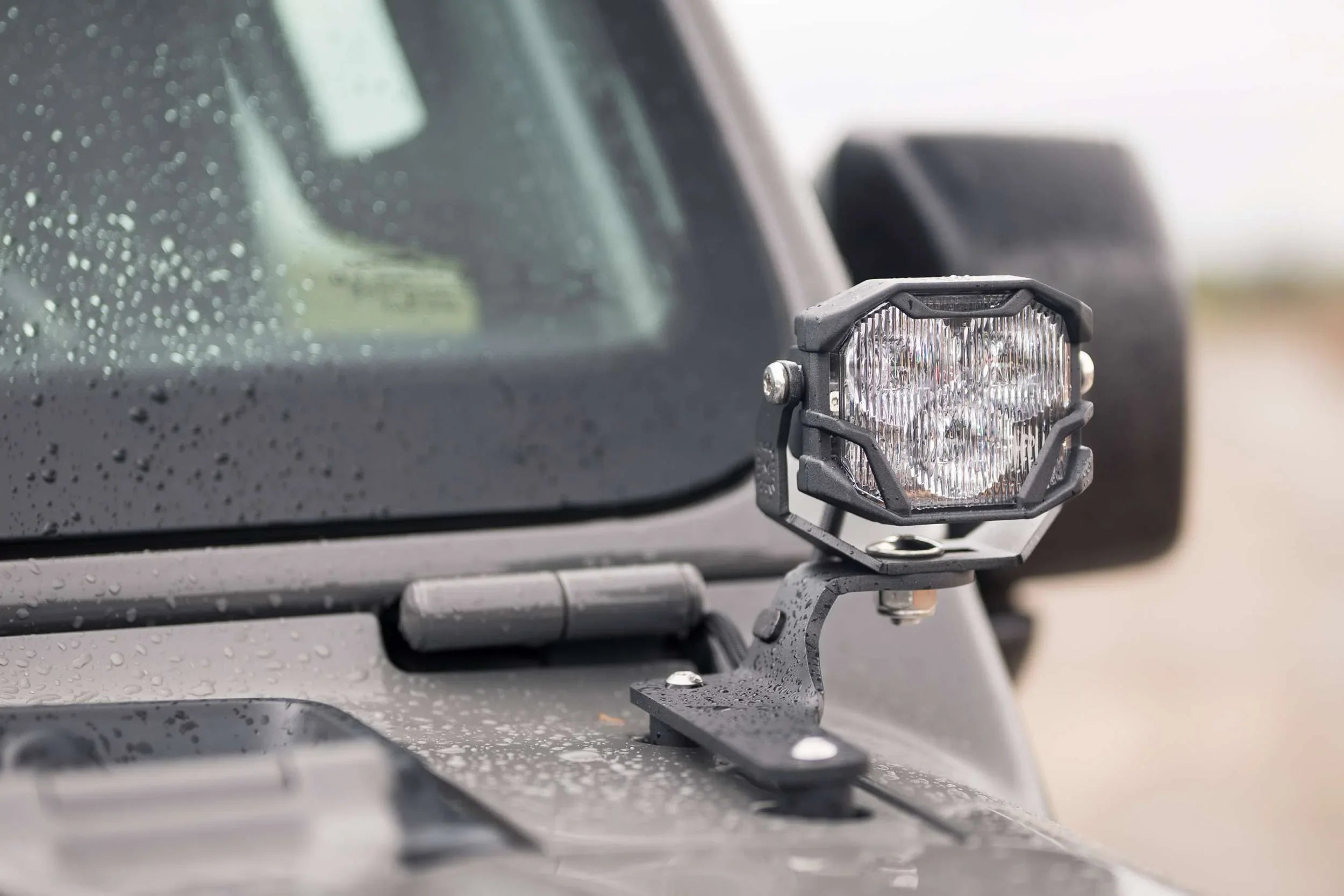 LED off-road pod light mounted on a Jeep hood, with water droplets on the vehicle