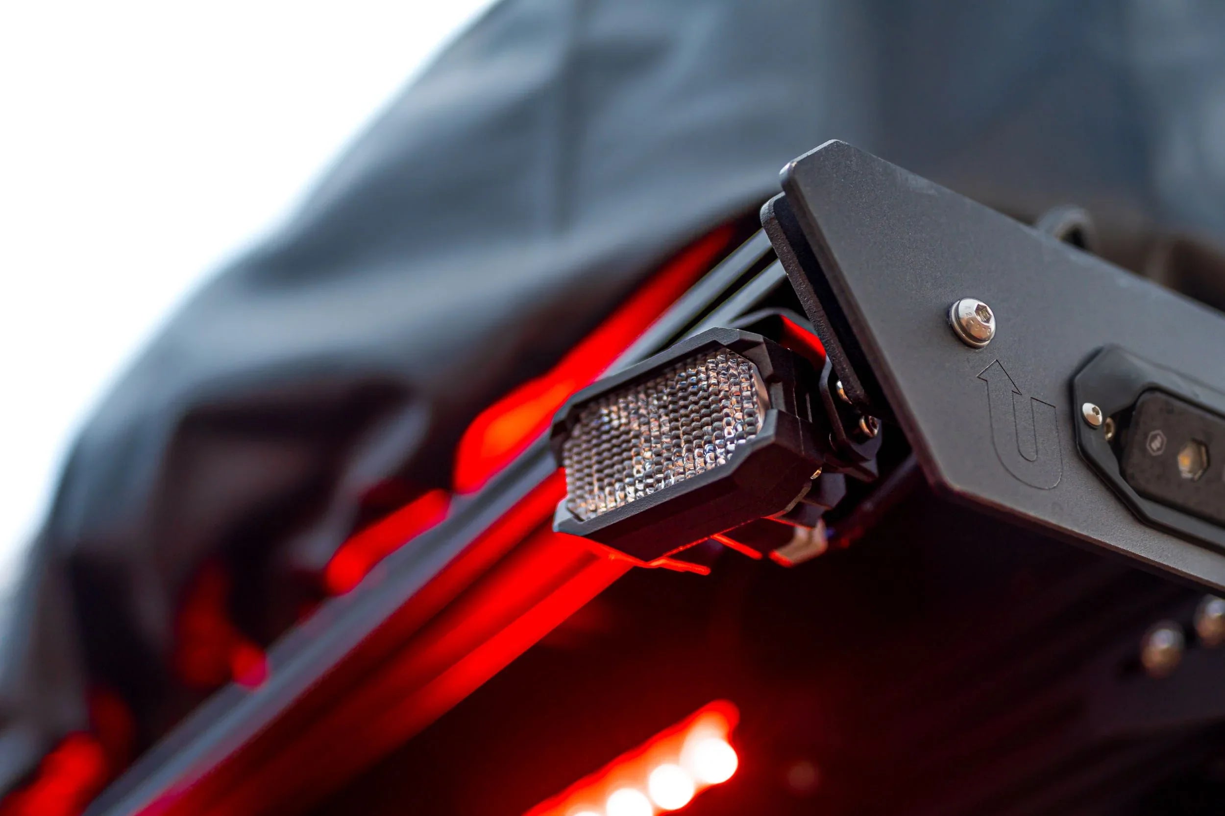 Close-up of LED accessory light mounted on overlanding vehicle rack with red illumination