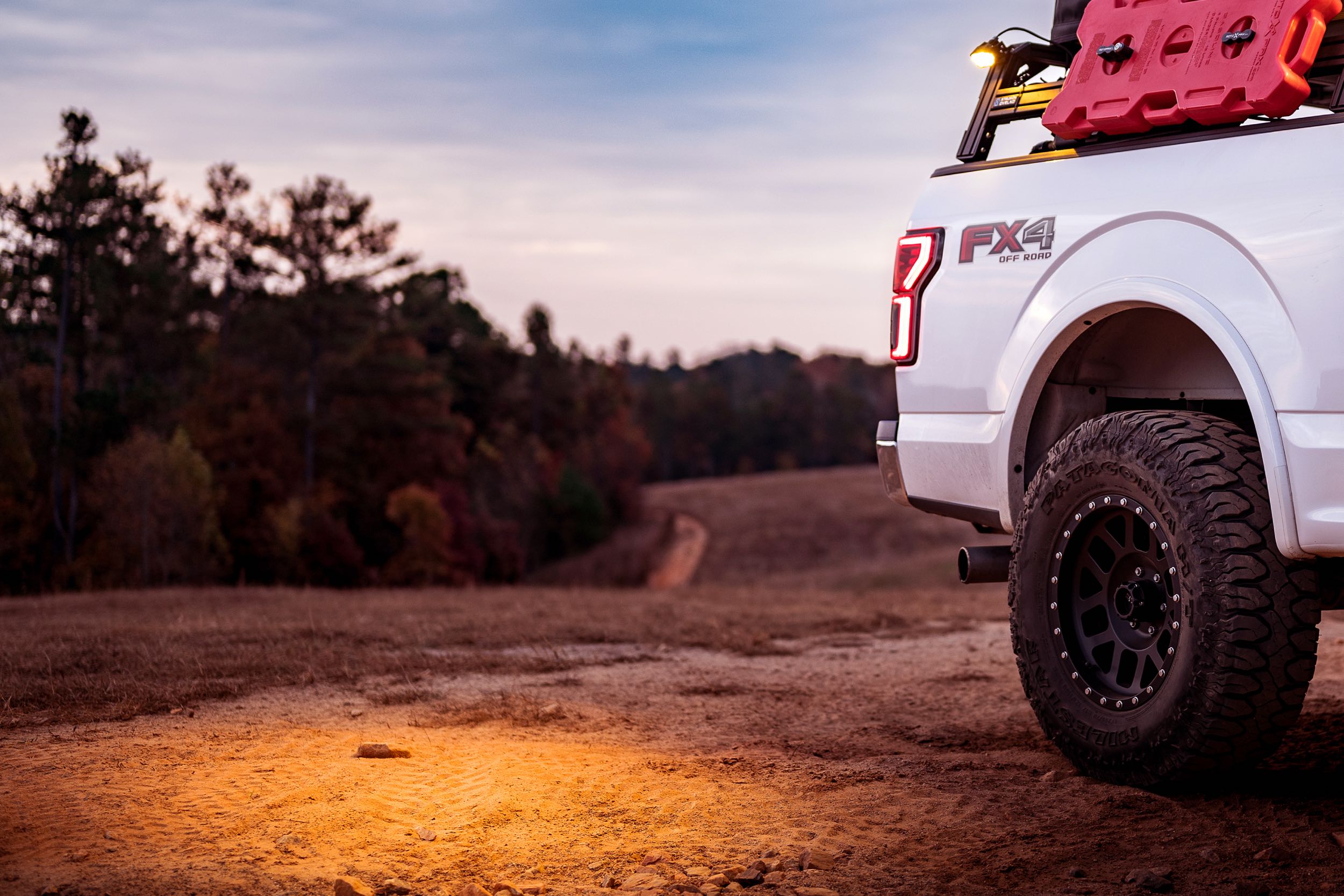Off-road truck with camping gear and LED light parked on a dirt trail at sunset