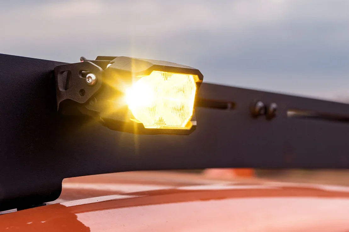 Yellow LED off-road light mounted on vehicle roof rack, illuminated at dusk
