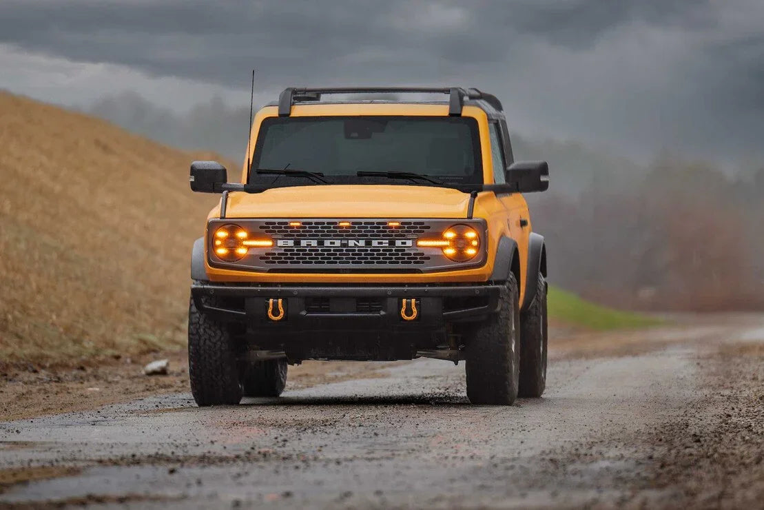 Yellow Ford Bronco SUV with off-road accessories on a muddy outdoor trail
