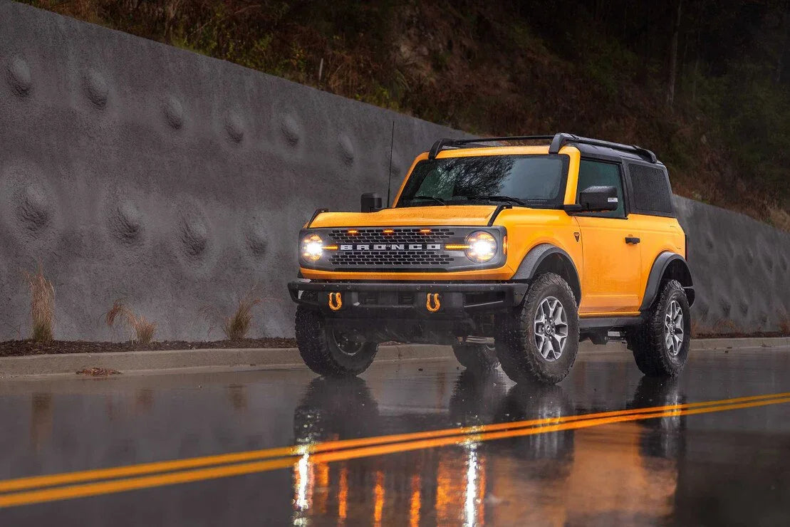 Yellow Ford Bronco off-road SUV parked on wet road, geared for adventure and overlanding.