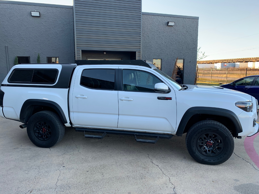 White Toyota Tacoma TRD Pro with black camper shell, parked outside industrial building