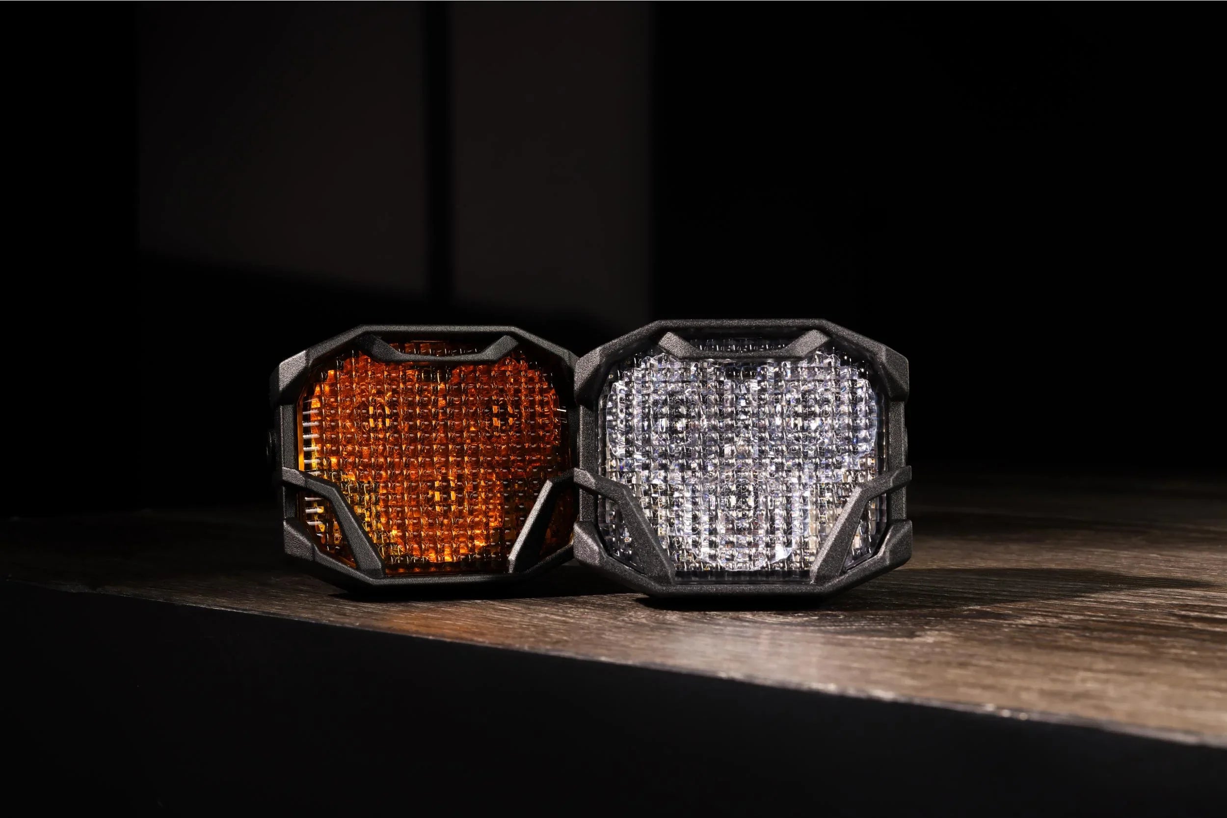 Amber and white LED pod lights with rugged black housings for off-road vehicles on wood surface