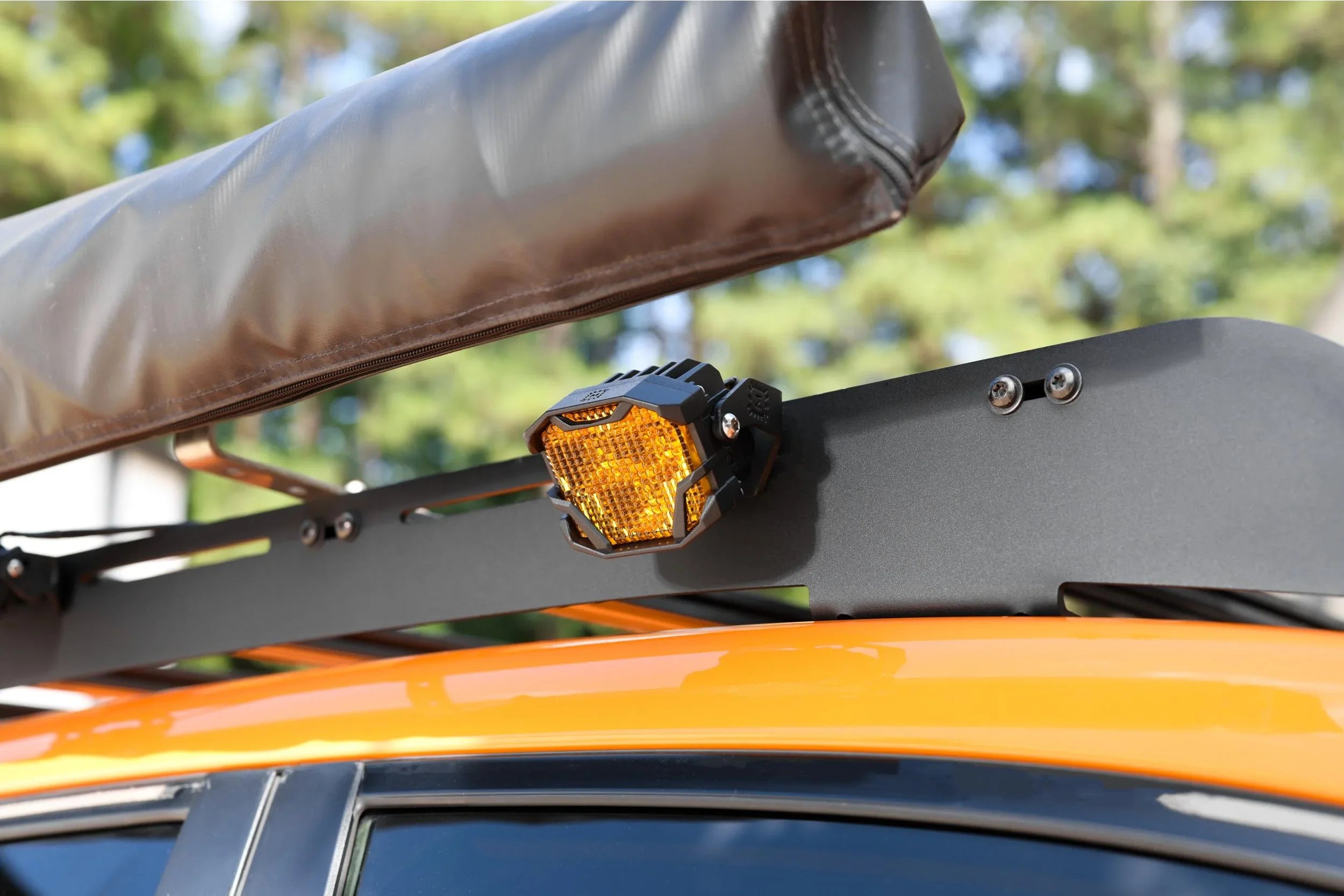 Amber off-road LED light mounted on roof rack of orange overlanding vehicle