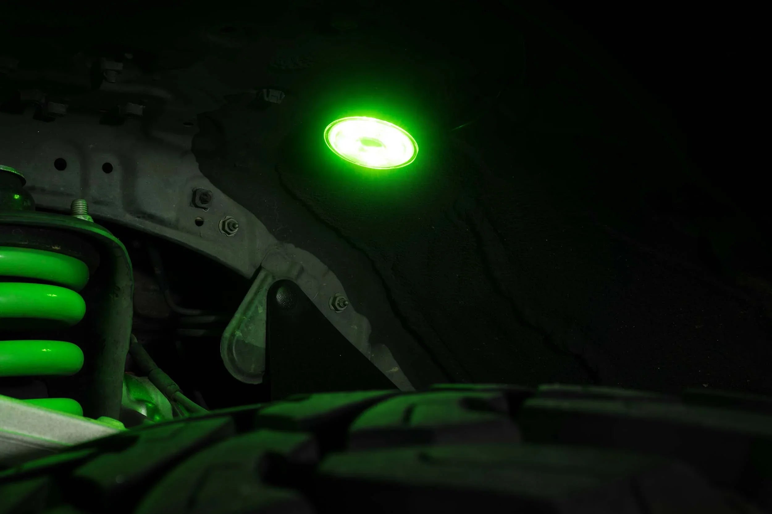 Green LED rock light installed above truck suspension and tire for off-road visibility