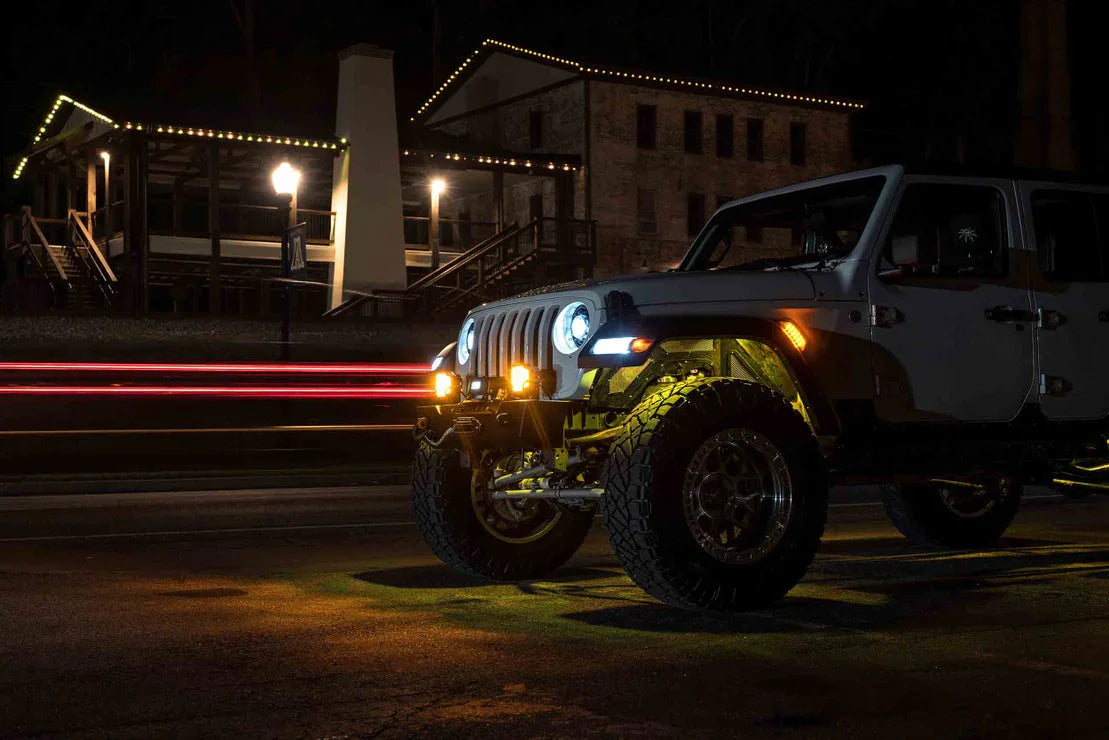Lifted Jeep Wrangler with off-road lights and large tires parked at night in front of a lit building