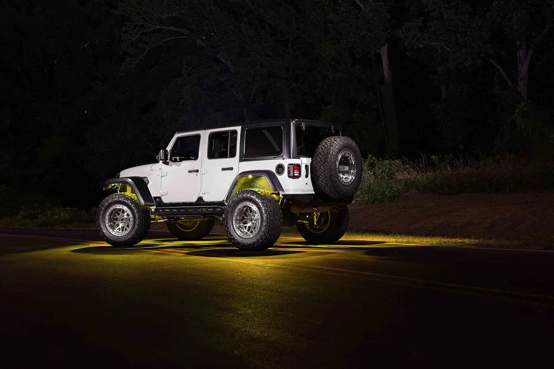 White Jeep Wrangler with off-road tires and underglow lights parked on a dark road at night