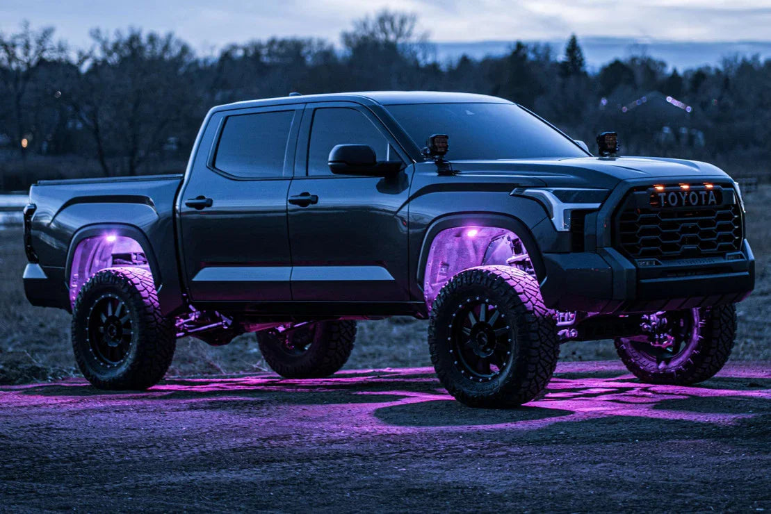 Lifted Toyota Tundra truck with off-road tires and purple underglow lights outdoors at dusk