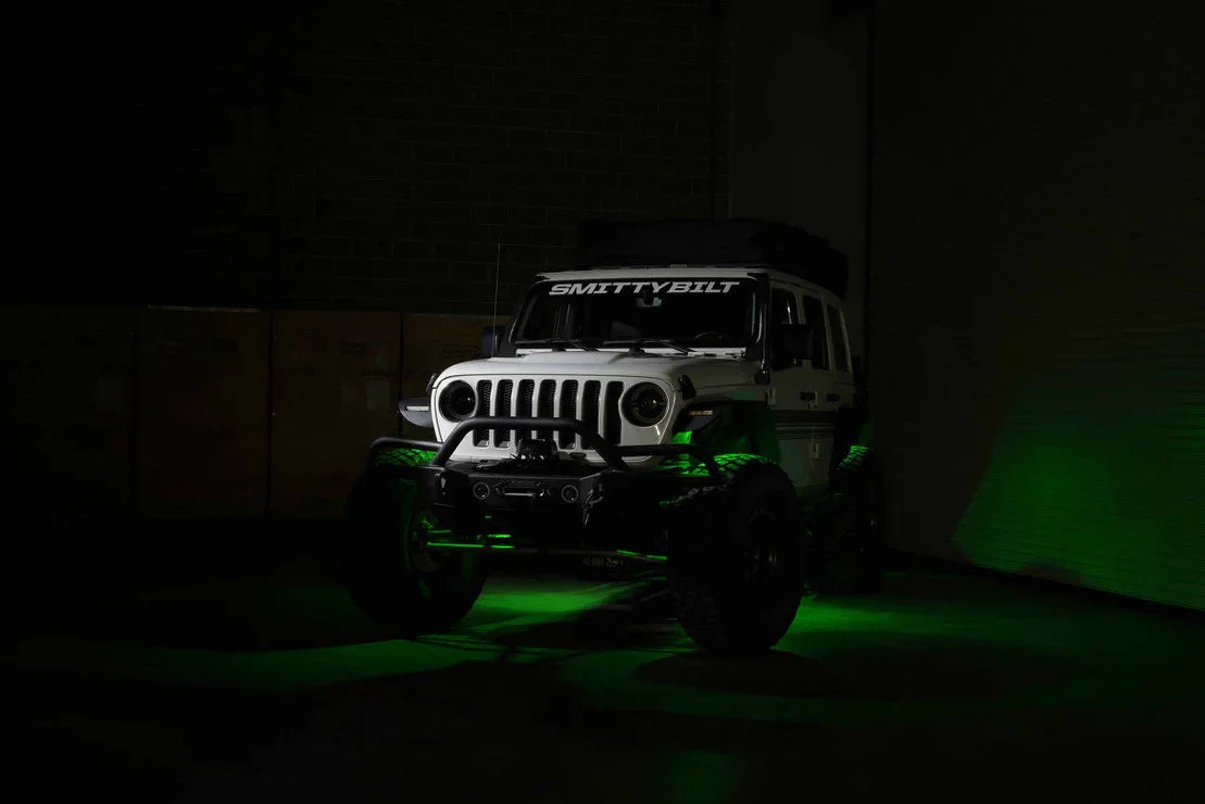 Lifted white Jeep Wrangler with off-road gear and green accent lighting in a dark garage