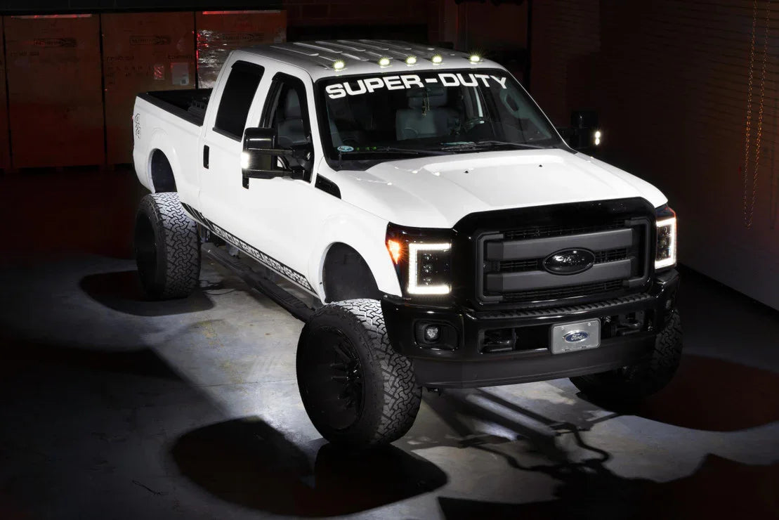 White Ford Super Duty truck with off-road tires and roof lights in a garage setting