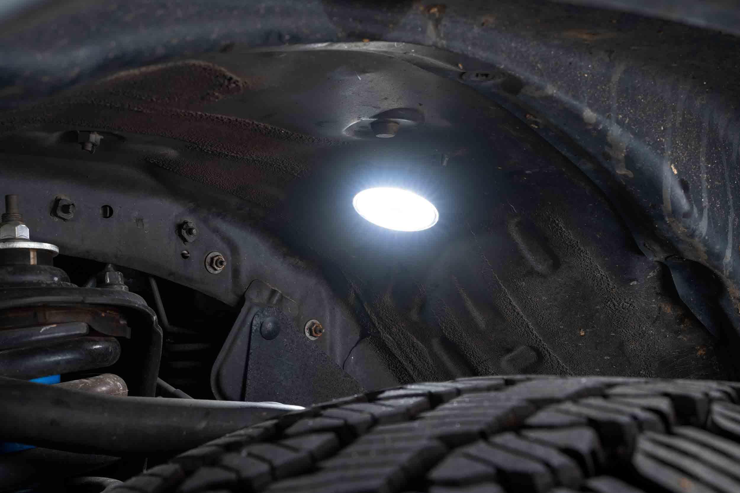 Bright LED rock light installed in vehicle wheel well, illuminating suspension and tire