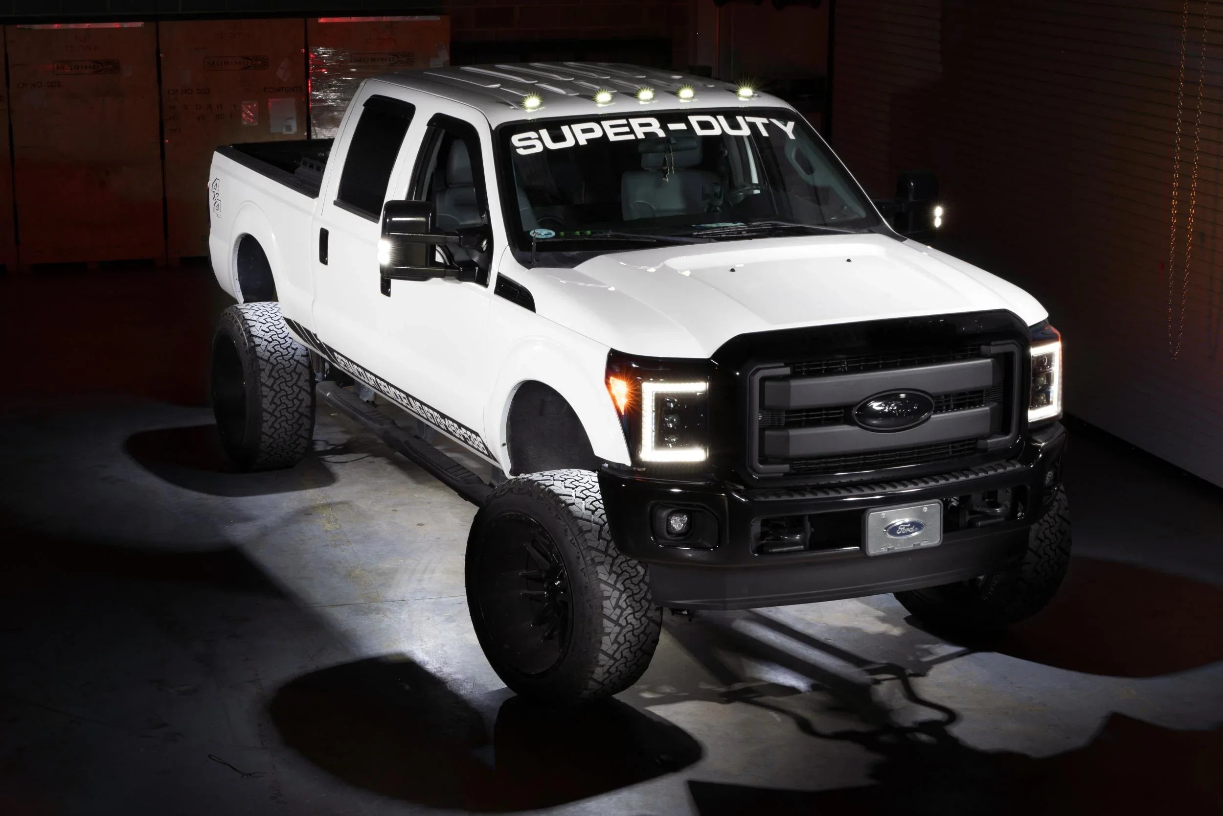 Lifted white Ford Super Duty truck with LED lights and off-road tires in a garage setting