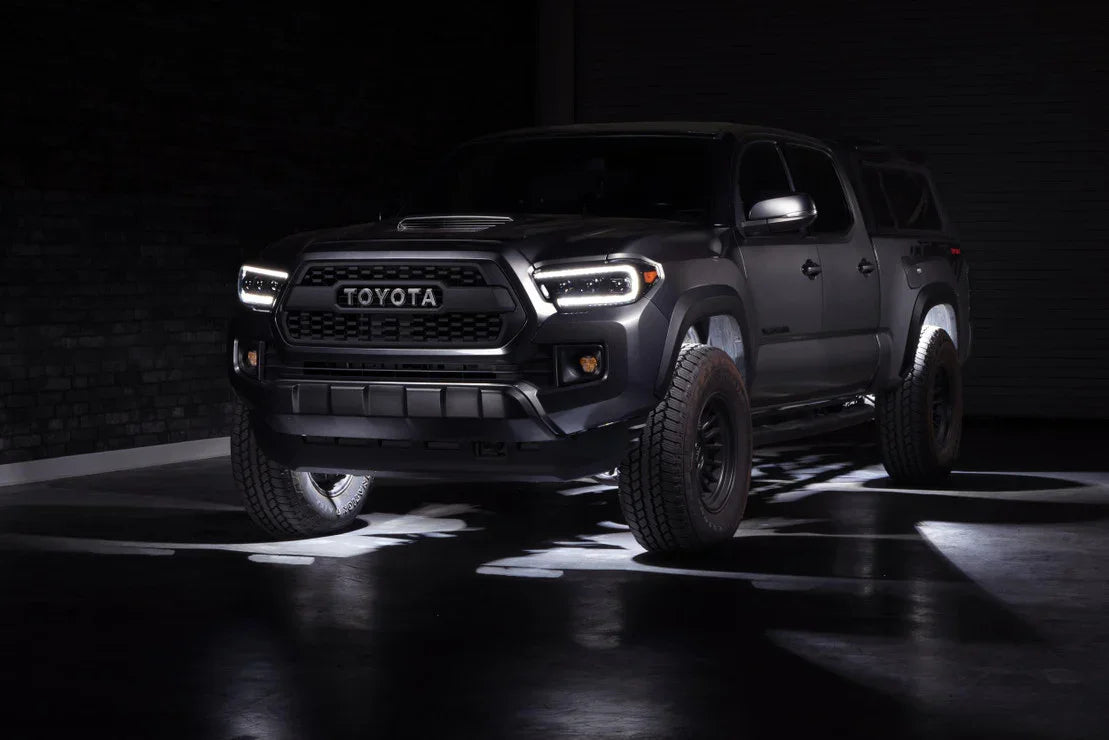 Black Toyota Tacoma with off-road tires and LED headlights in a dimly lit garage