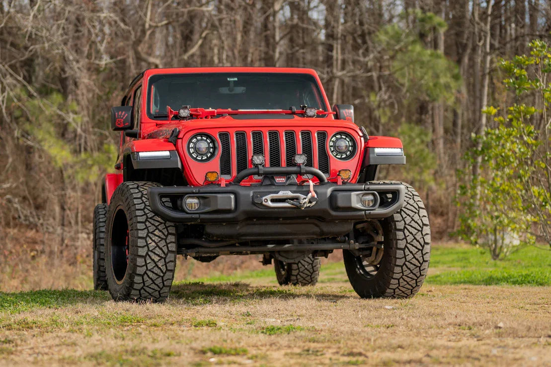 Red Jeep Wrangler with off-road tires, custom LED headlights, and front winch in outdoor setting