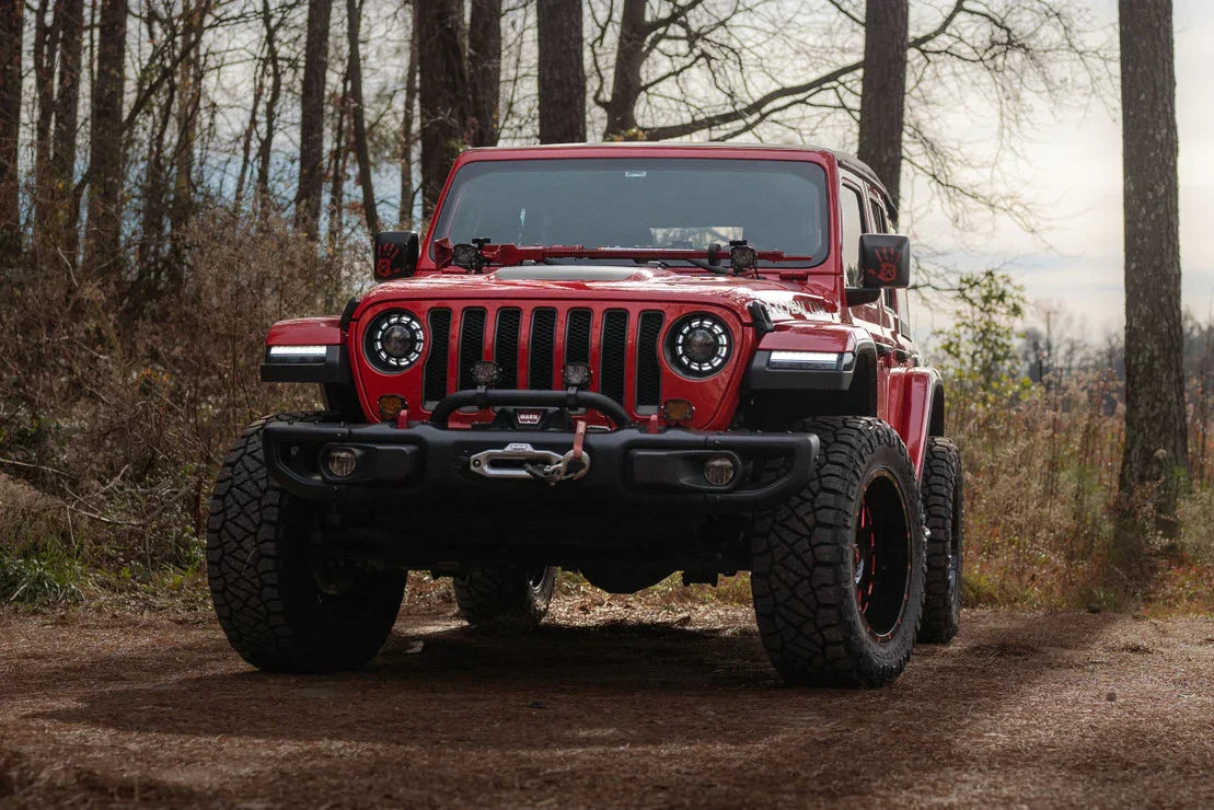 Red Jeep Wrangler with off-road tires, winch, LED halo headlights in a forest setting