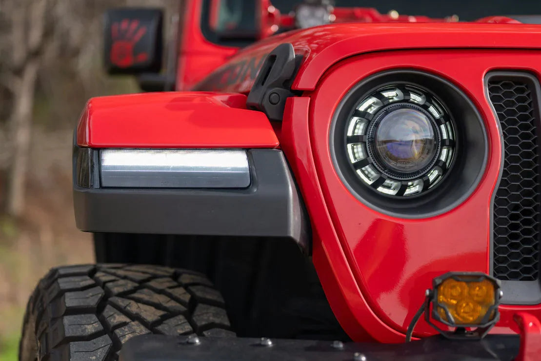 Close-up of red Jeep front end with rugged off-road tire, LED headlight, and amber light