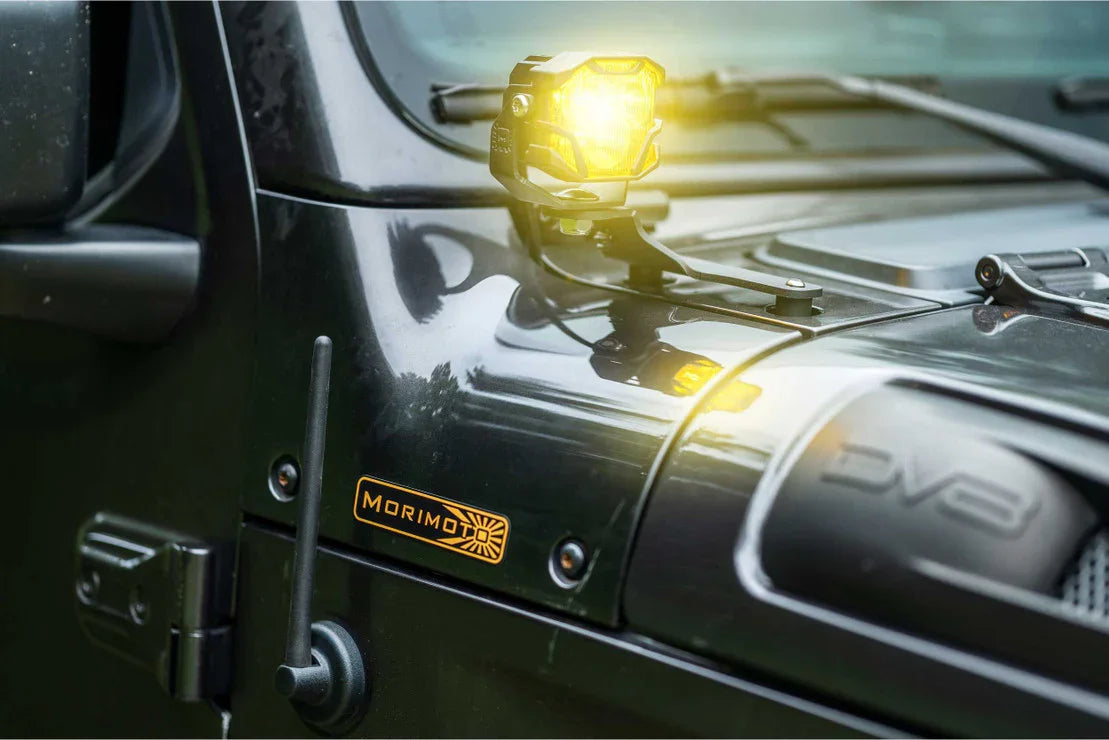 Yellow LED pod light mounted on off-road vehicle hood with MORIMOTO badge, close-up