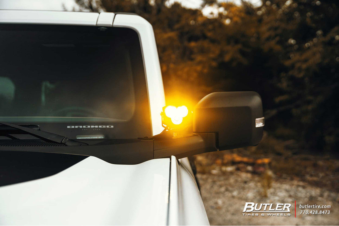 Ford Bronco with bright amber off-road pod light mounted on mirror, outdoor setting