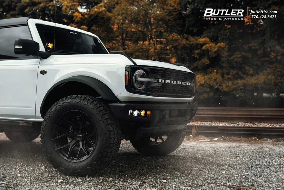 White Ford Bronco with off-road tires parked near railroad tracks, showcasing rugged vehicle accessories.