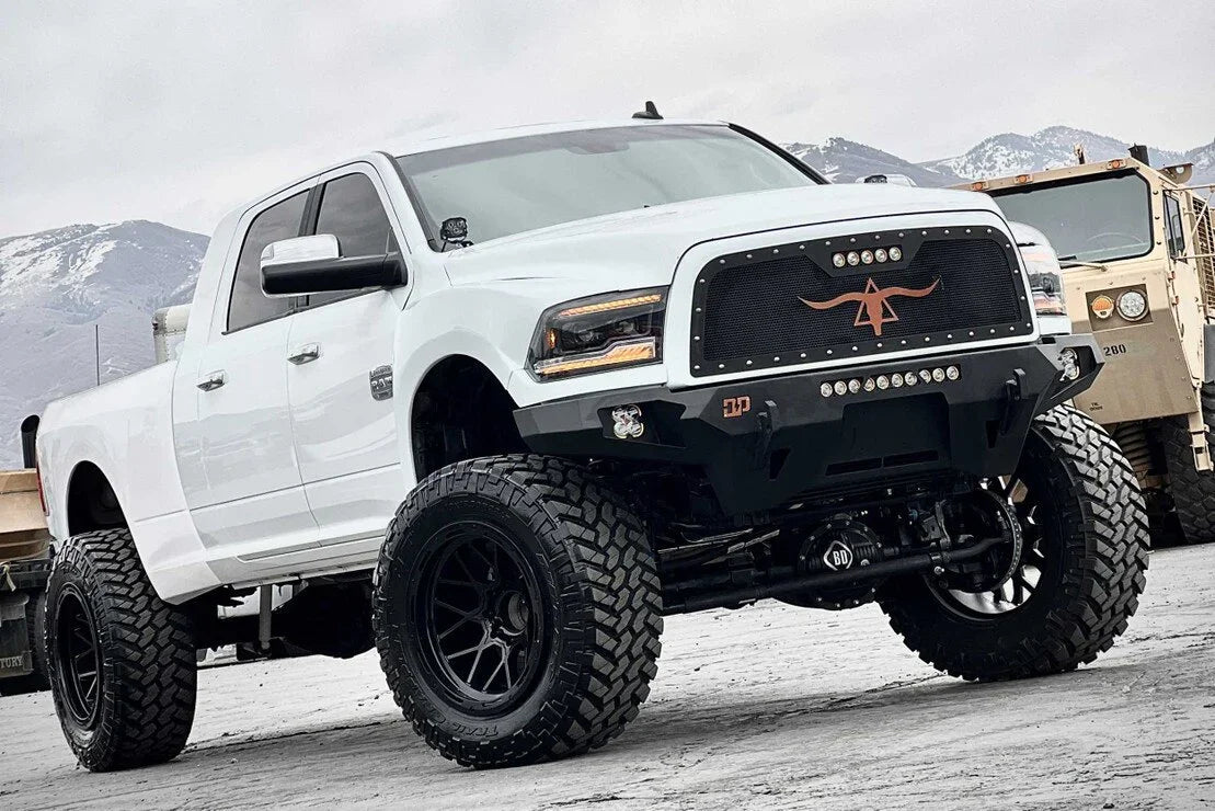 Lifted white Ram truck with amber XB LED headlights and off-road tires in a mountain setting