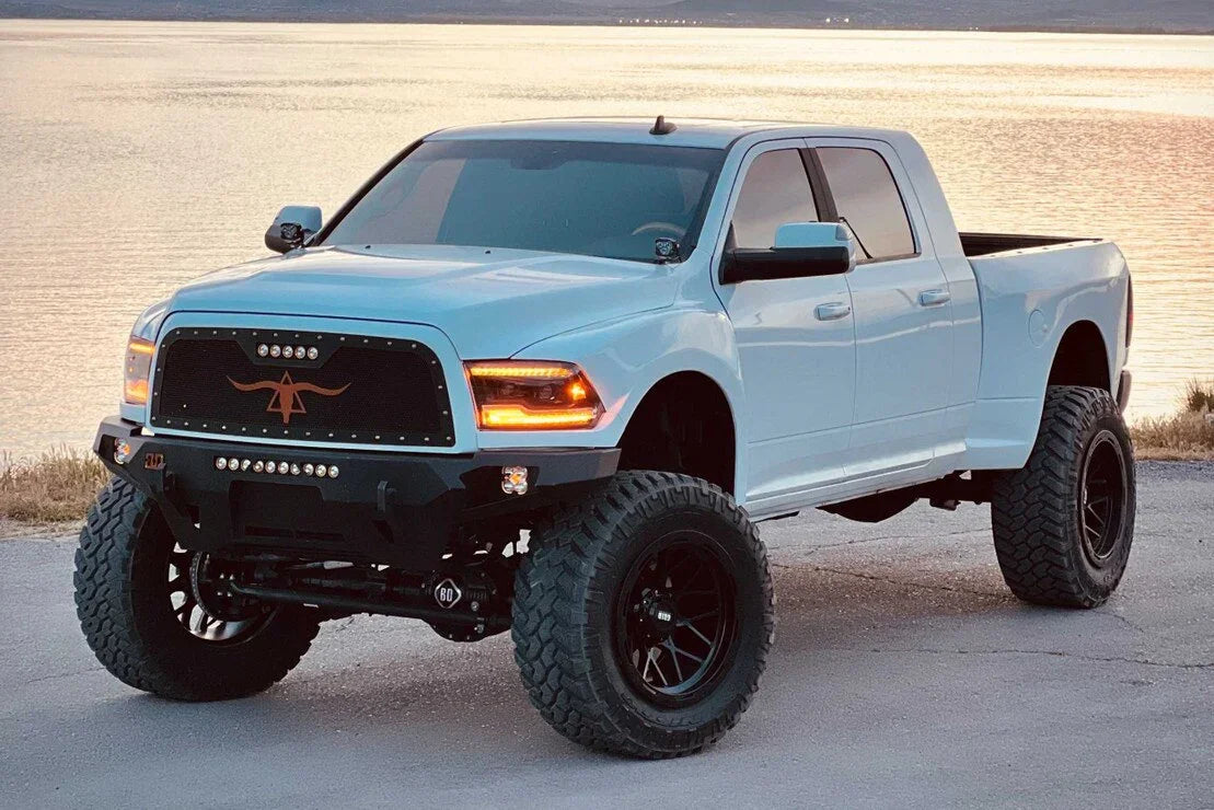 Lifted Ram truck with amber XB LED headlights, off-road tires and custom grille by a lake