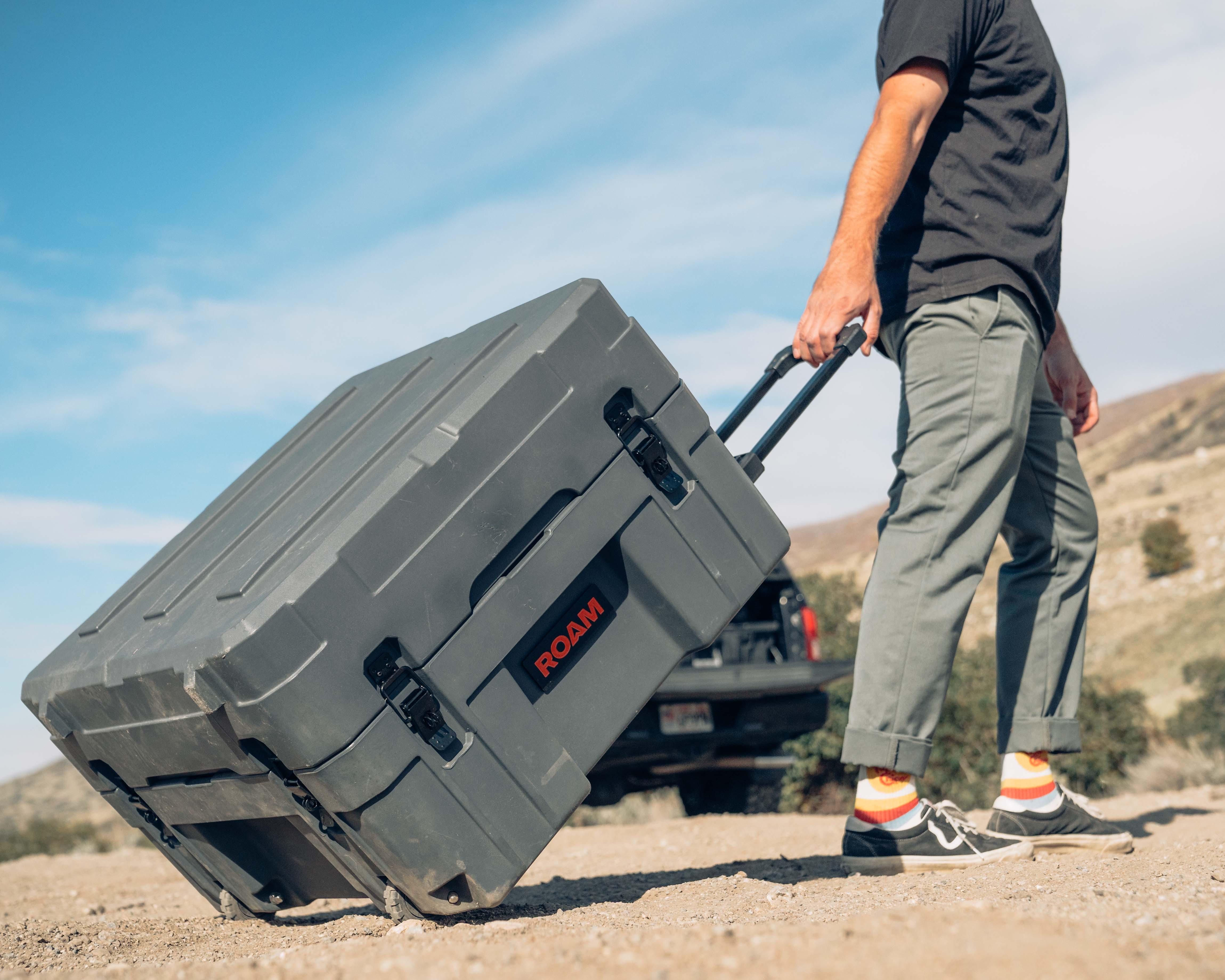 Person pulling a large rugged storage case with wheels outdoors for overlanding or camping gear.