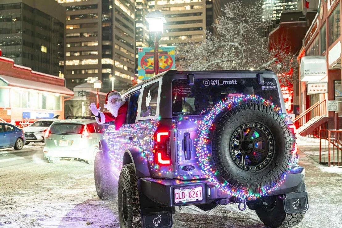 Jeep Wrangler decorated with Christmas lights, Santa waving, snowy city street at night