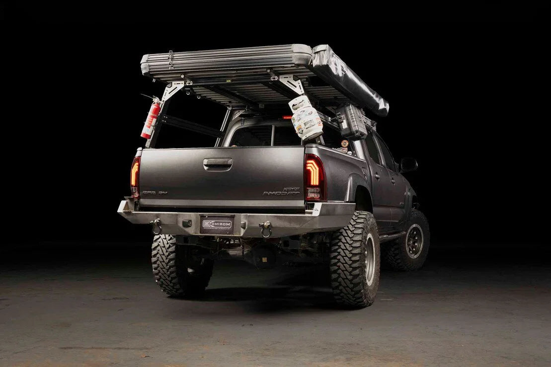 Overland Toyota Tacoma with off-road tires, roof rack, awning, propane tank, and gear accessories