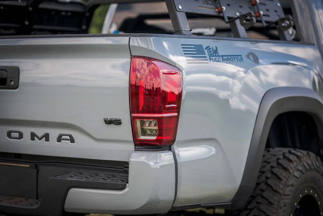 Toyota Tacoma rear with V6 badge, red tail light, off-road rack, and rugged tire