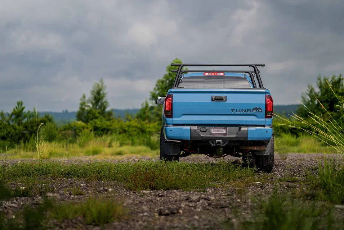 Blue Toyota Tundra with overlanding rack parked on a gravel trail in a green outdoor setting
