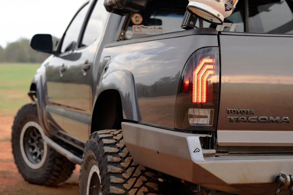 Toyota Tacoma with aftermarket clear tail lights and off-road tires on a dirt trail