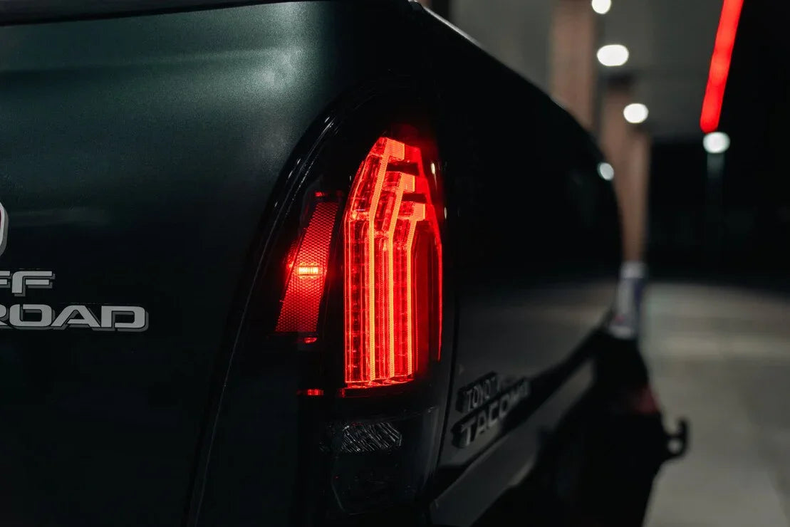 Toyota Tacoma truck with illuminated clear LED tail lights, off-road decal visible at night