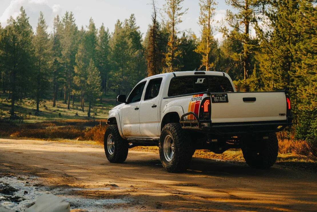 Lifted white Toyota Tacoma TRD pickup with aftermarket tail lights on a forest dirt road