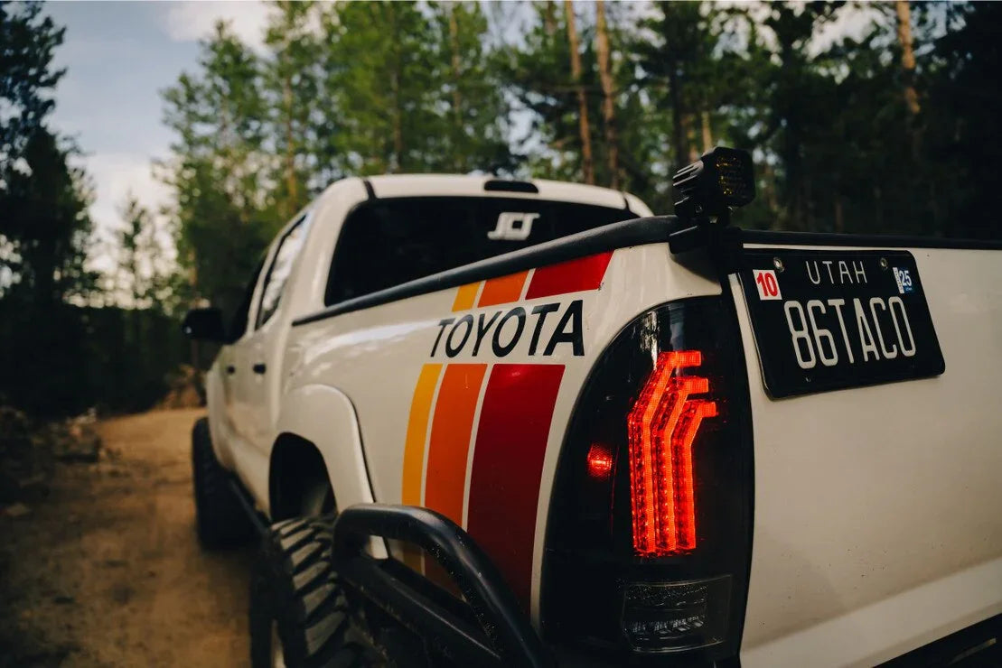 Toyota Tacoma with clear LED tail lights and retro stripes on an off-road forest trail