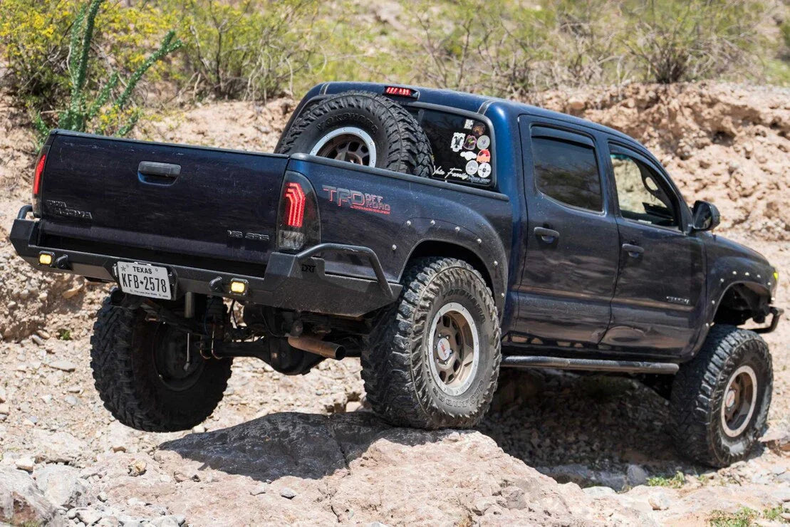 Lifted Toyota Tacoma off-roading on rocky terrain, featuring clear tail lights and rugged tires.