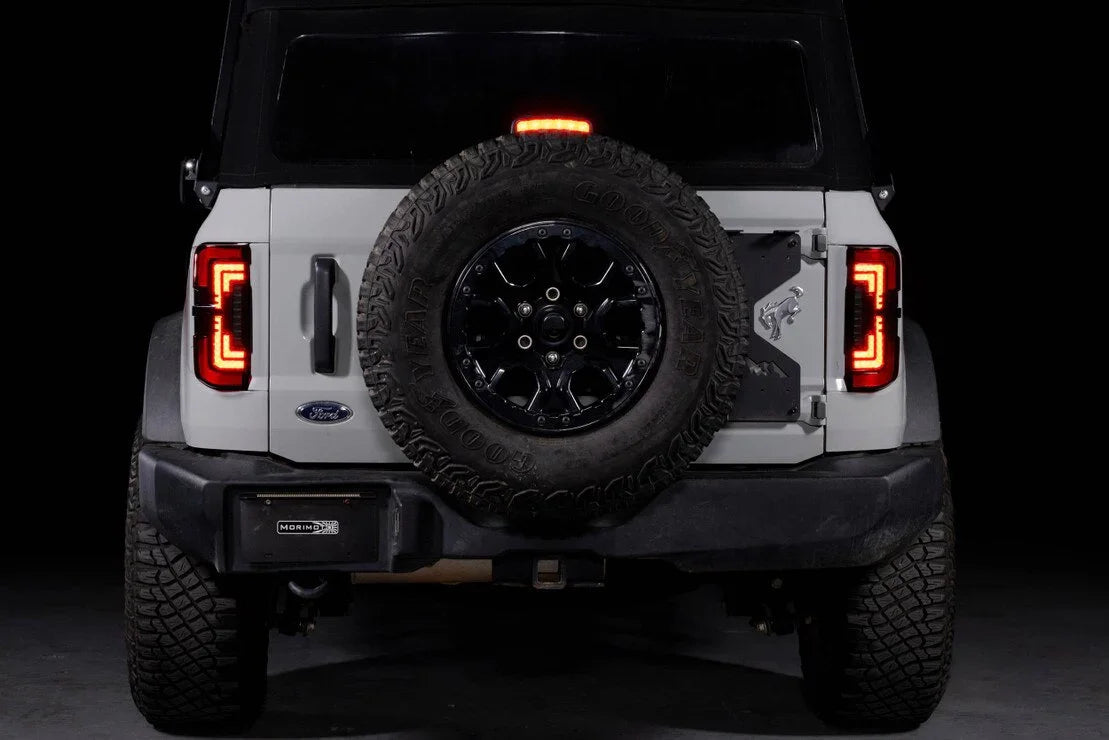 Rear view of a white Ford Bronco with aftermarket red smoked LED tail lights and spare tire.
