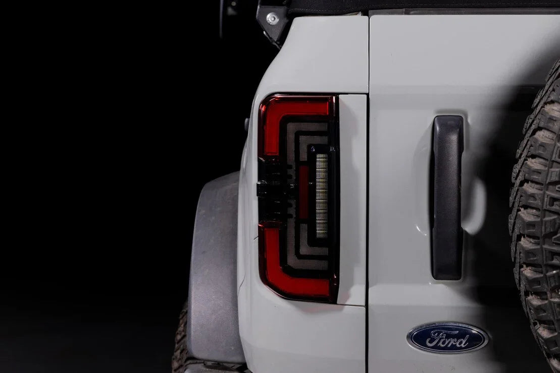Red smoked LED tail light on white Ford Bronco rear, off-road tire visible