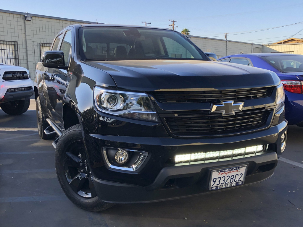 Black Chevrolet pickup truck with LED light bar and off-road accessories in parking lot