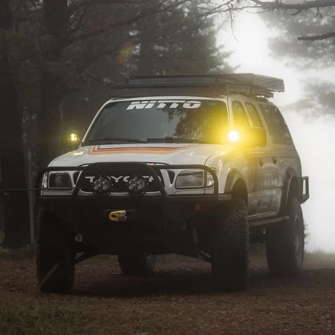 Toyota Tacoma with ditch light brackets and yellow LED lights in a foggy forest