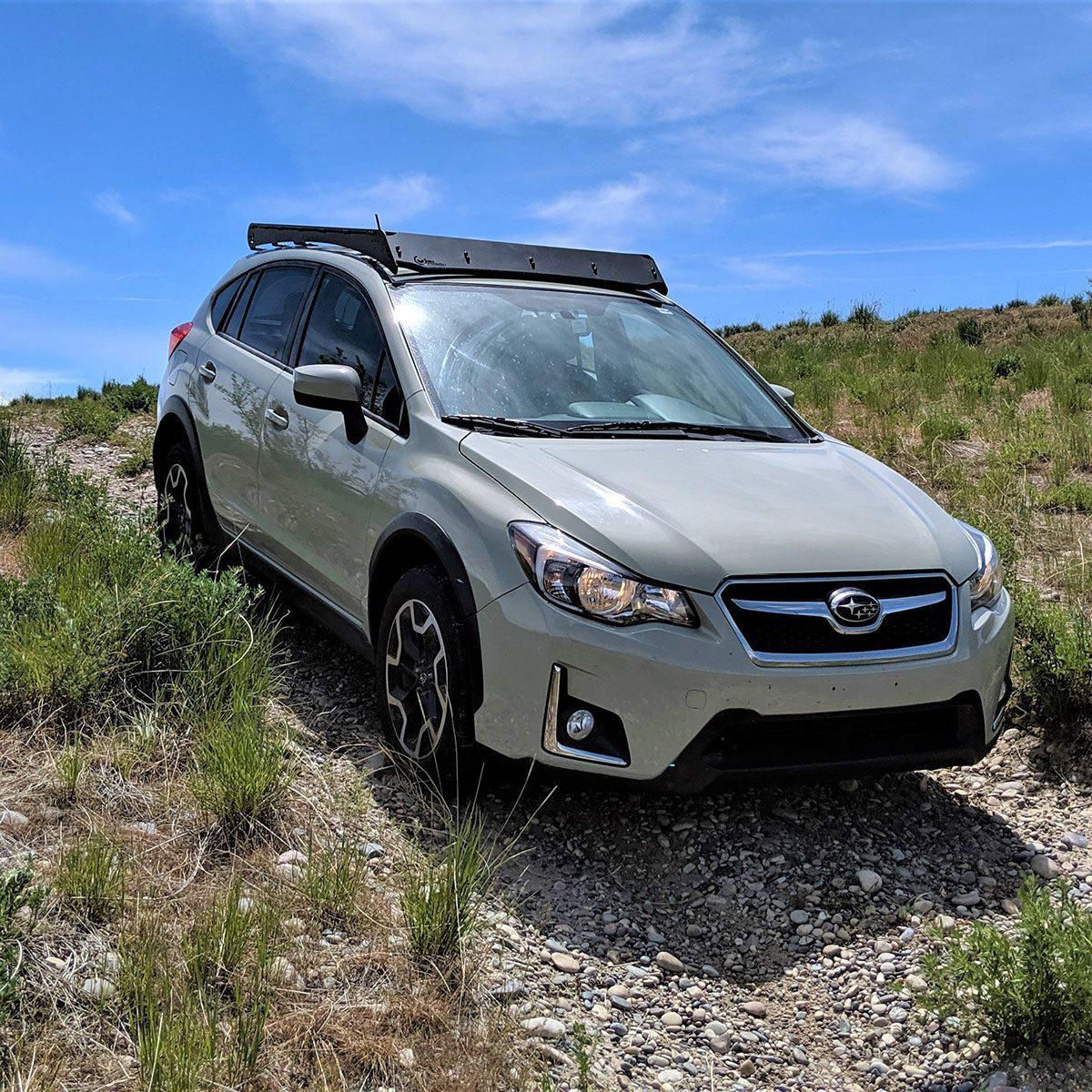 Subaru Crosstrek with roof rack driving off-road on a rocky trail in daylight