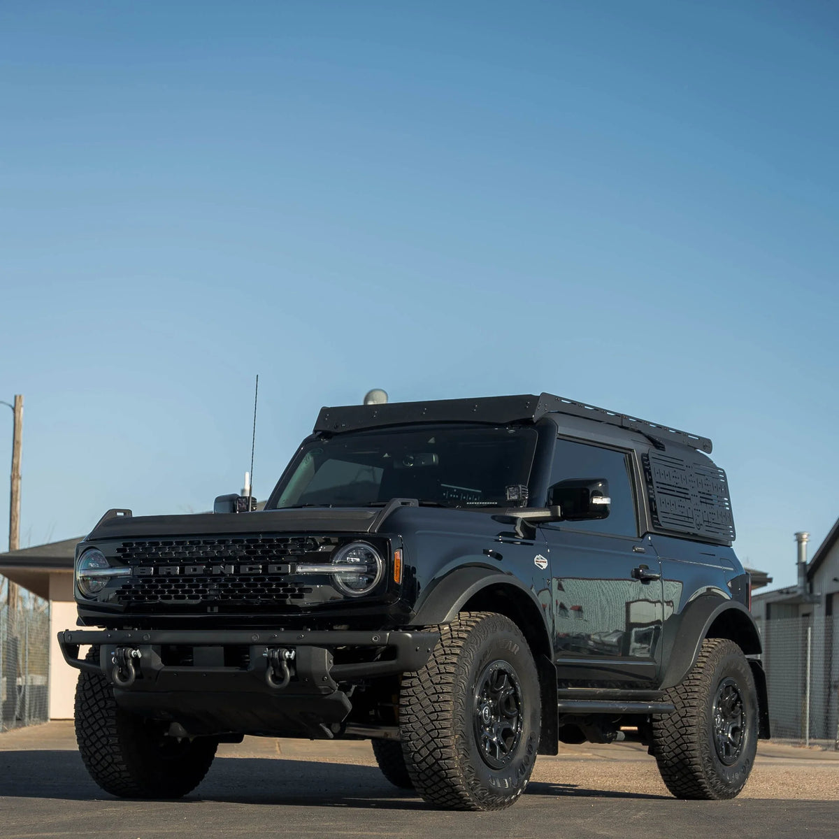 Black 2-door Ford Bronco with off-road window panel and roof rack under blue sky