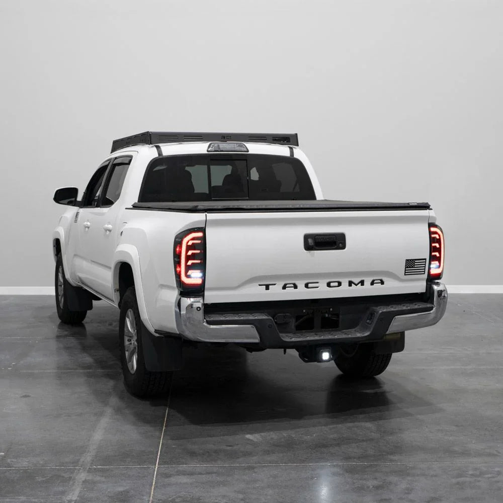 White 2018 Toyota Tacoma with aftermarket LED tail lights in a studio setting, rear angle view