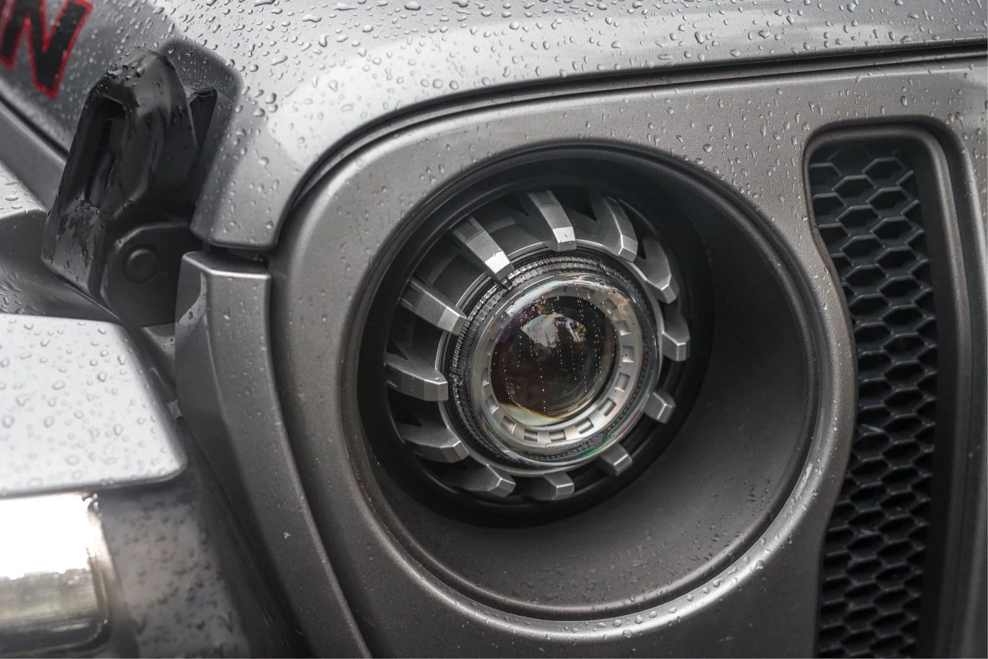Close-up of Jeep Wrangler JL LED headlight adapter on wet front grille