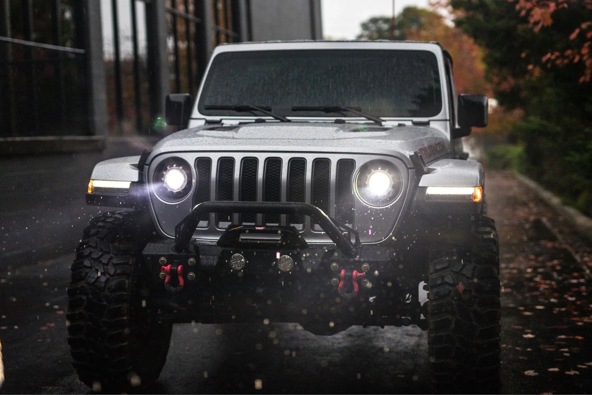 Front view of a Jeep Wrangler JL with illuminated 7-inch LED headlights on a wet road